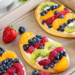 three mini fruit pizzas topped with fresh fruiton a baking sheet