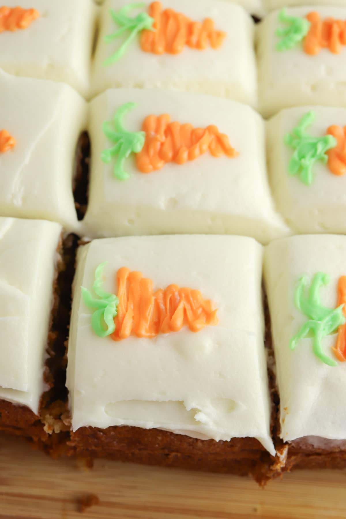 several square cut carrot cake bars topped with cream cheese icing each with a icing shaped carrot