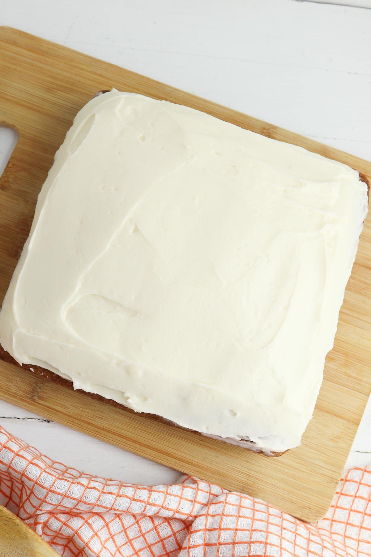 square carrot cake topped with cream cheese frosting on a wood cutting board
