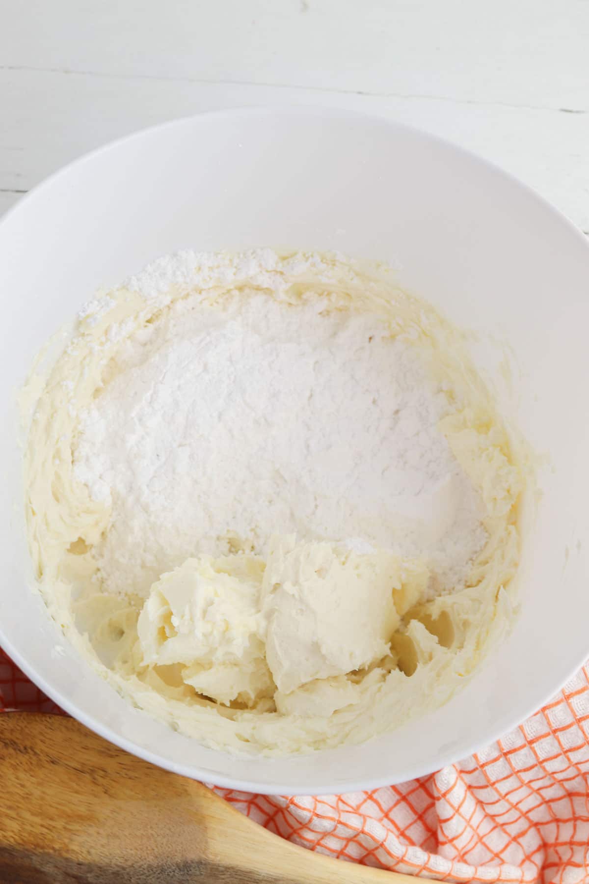 white mixing bowl with whipped cream cheese and powder sugar on top