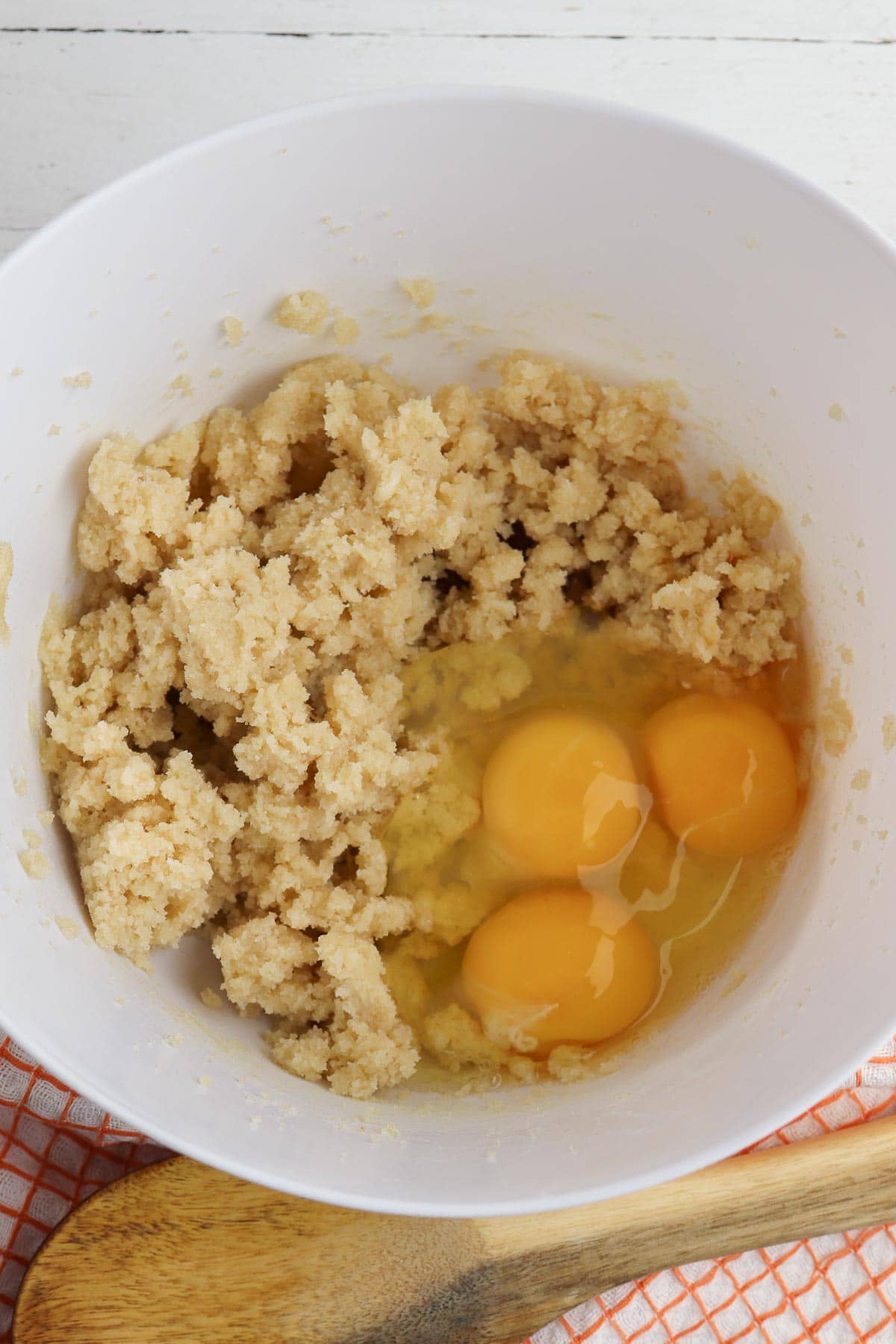 white mixing bowl with with three eggs on top of butter sugar mixture