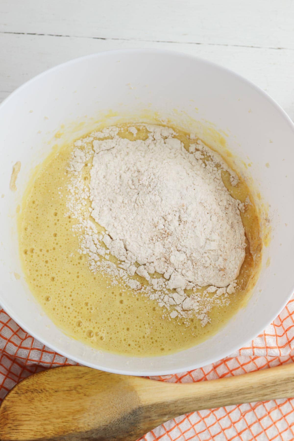 white mixing bowl with egg and sugar mixture topped with some all purpose flour