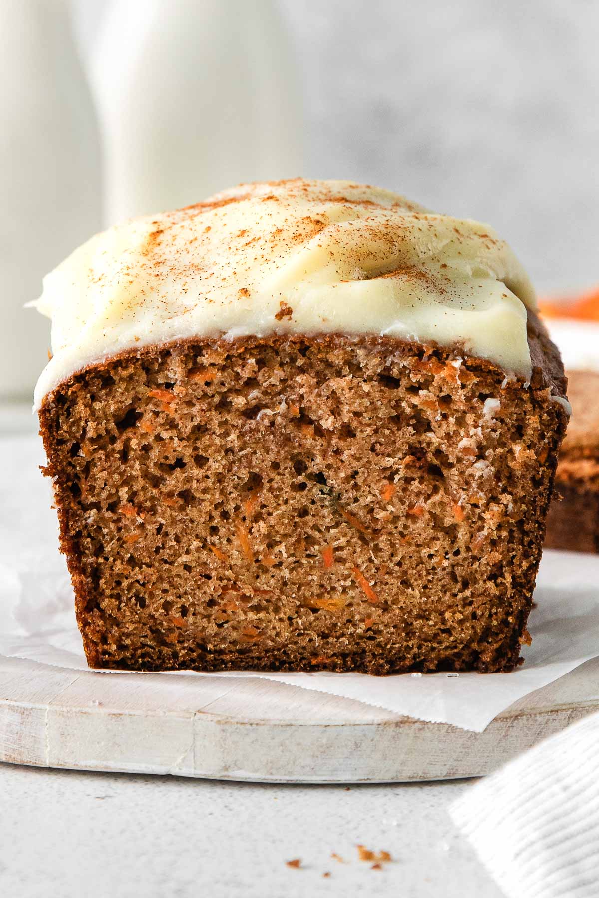 closeup of cut carrot cake loaf with cream cheese frosting on a white board