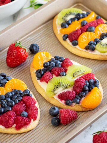 closeup of three fruit pizza cookies topped with cream cheese frosting and raspberries, blueberries, kiwi slices and mandarin oranges.