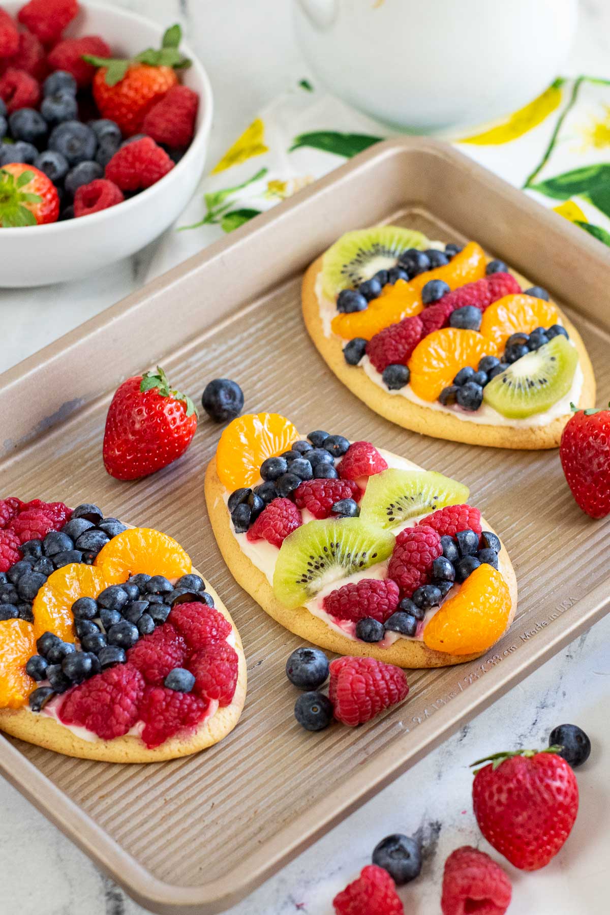 closeup of fruit pizza cookies with raspberries, blueberries and kiwi on a small baking sheet