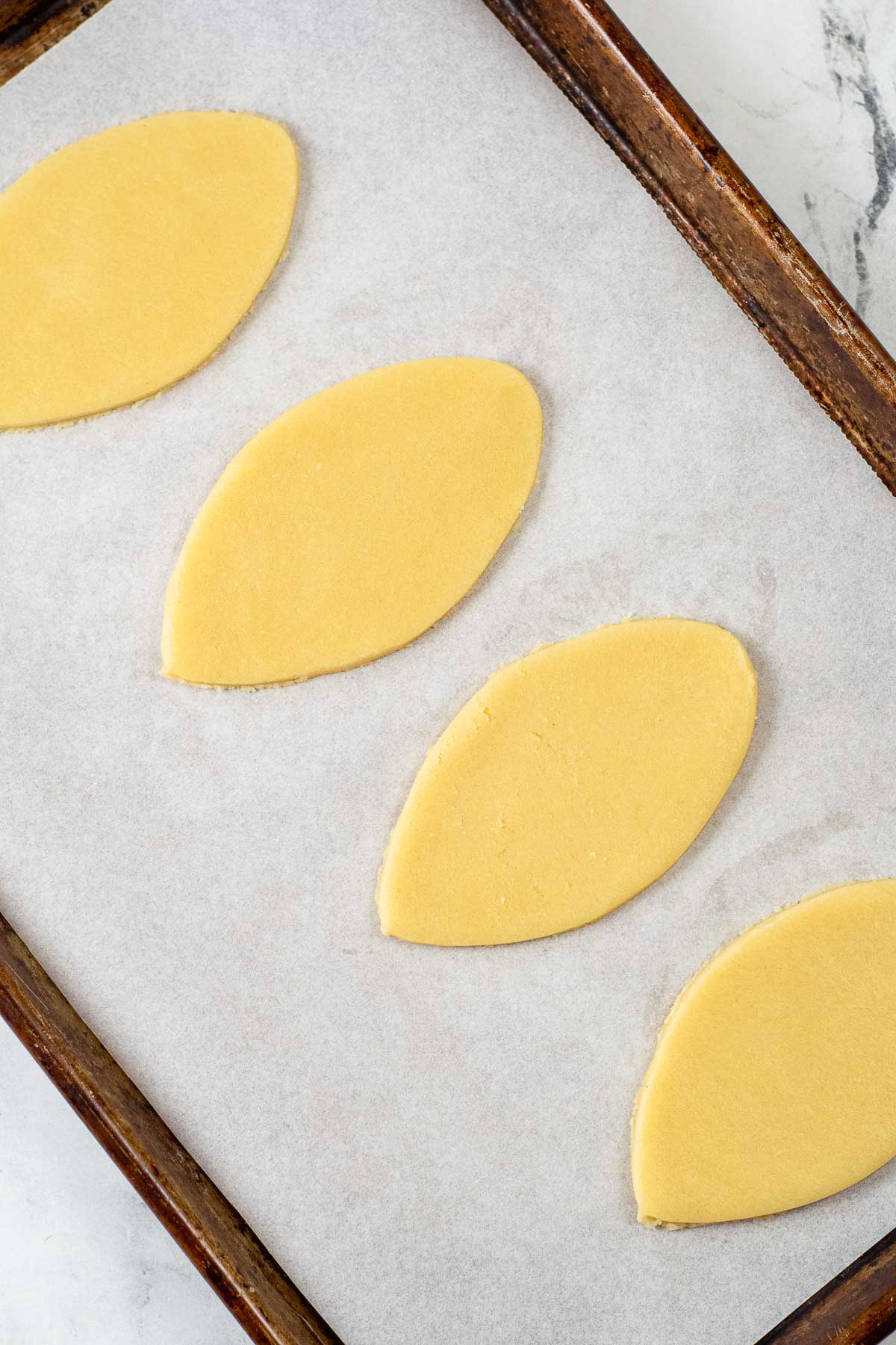 four egg shaped sugar cookie dough on a parchment lined baking sheet