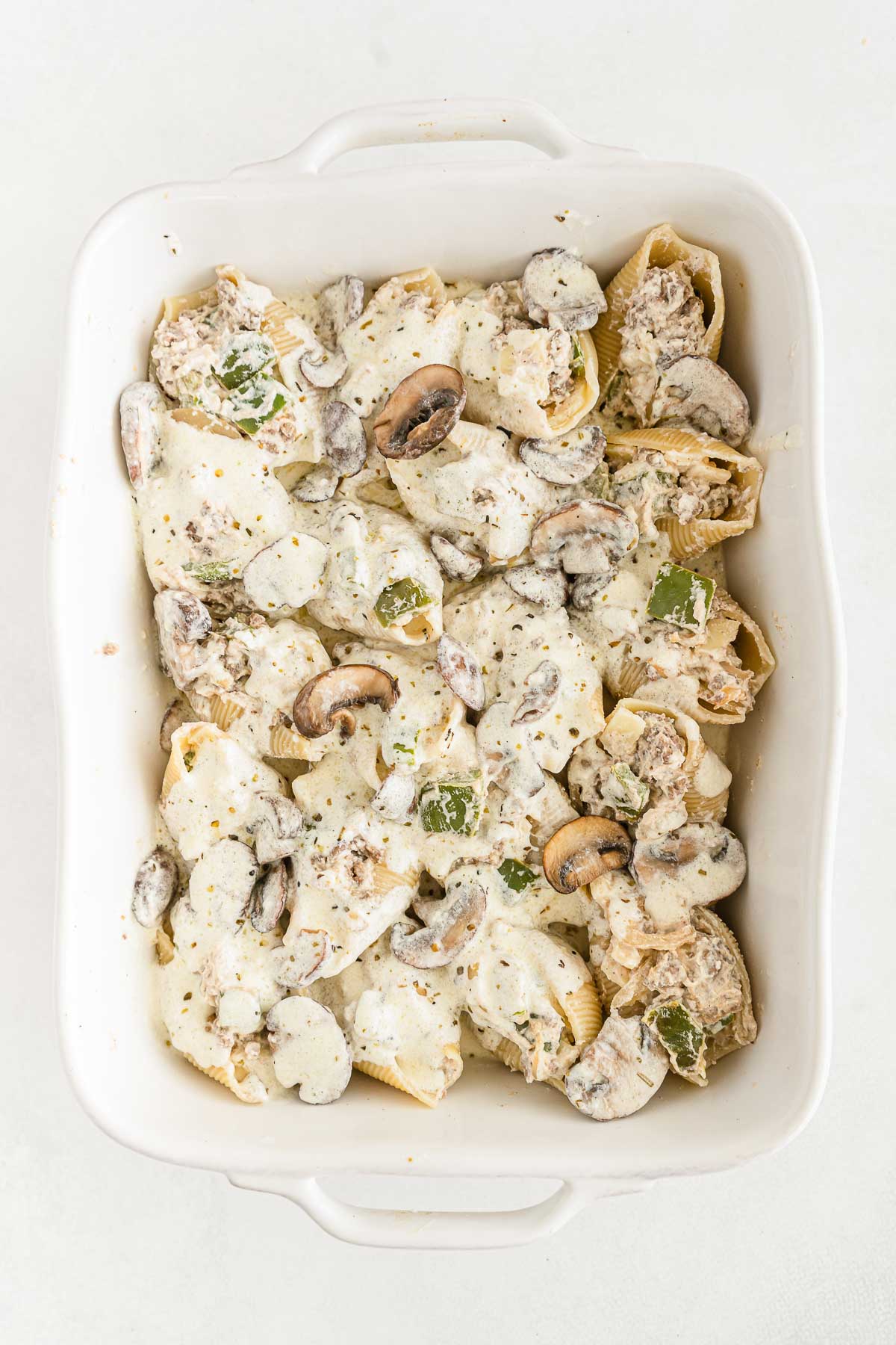 cheesesteak stuffed pasta shells topped with creamy alfredo sauce in a white casserole dish