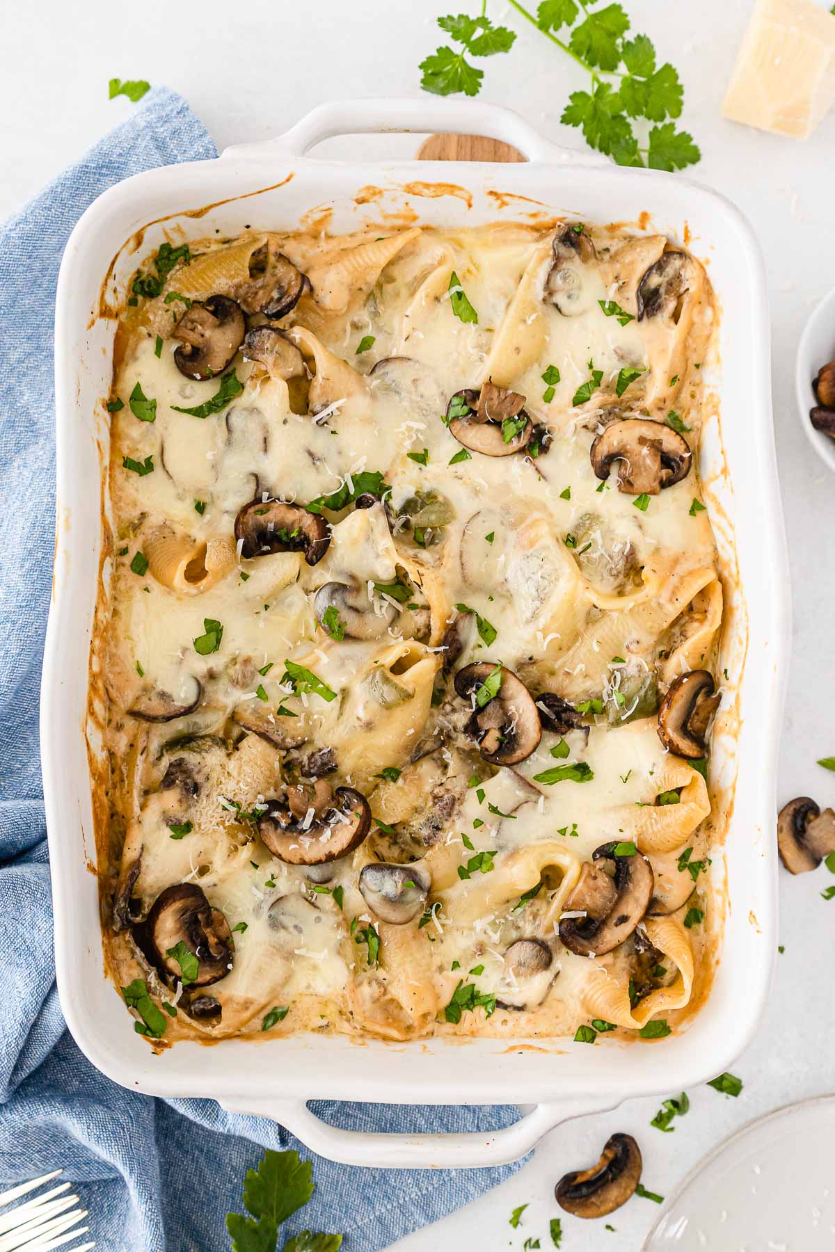 philly cheesesteak stuffed shells topped with cheese and mushrooms in white casserole dish