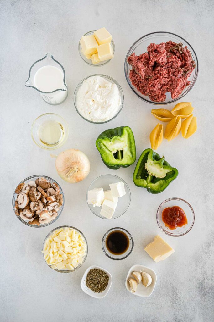 several glass bowls with ingredients for stuffed shells - hamburger, pasta shells, green pepper, fresh mushrooms, mozzarella cheese, garlic, spices