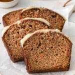 four slices of carrot cake loaf with cream cheese frosting on white parchment paper