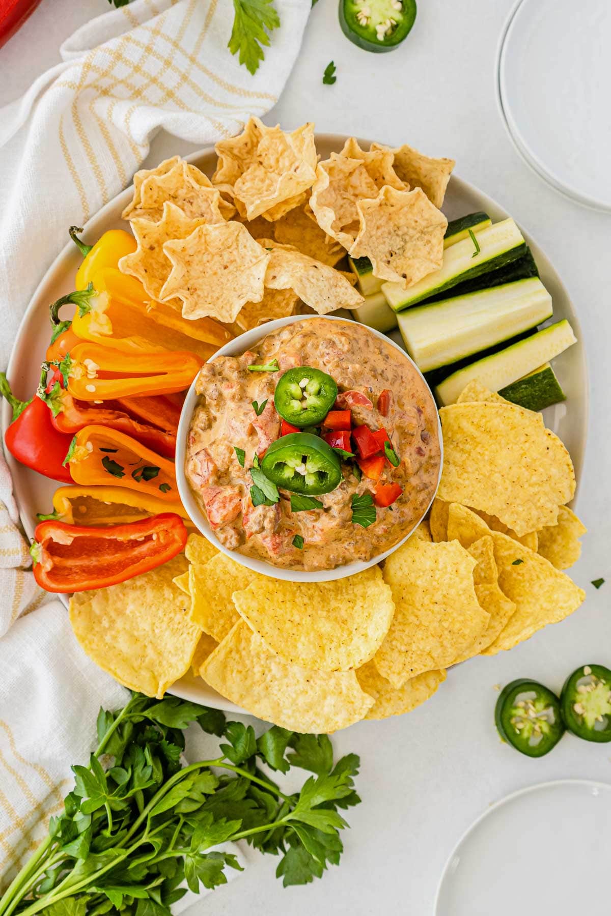 white bowl of rotel dip with meat surrounded by tortilla chips, sliced red peppers and zucchini