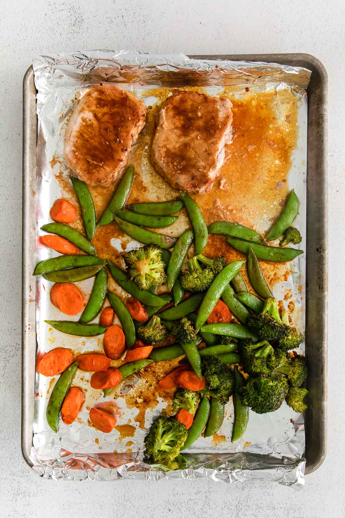 sheet pan with two pork chops,, broccoli and sugar snap peas baked with a soy sauce marinade