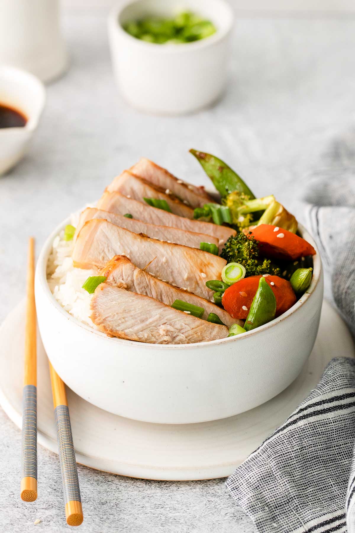 white bowl with sliced pork chop over white rice with vegetables and chopsticks on the side
