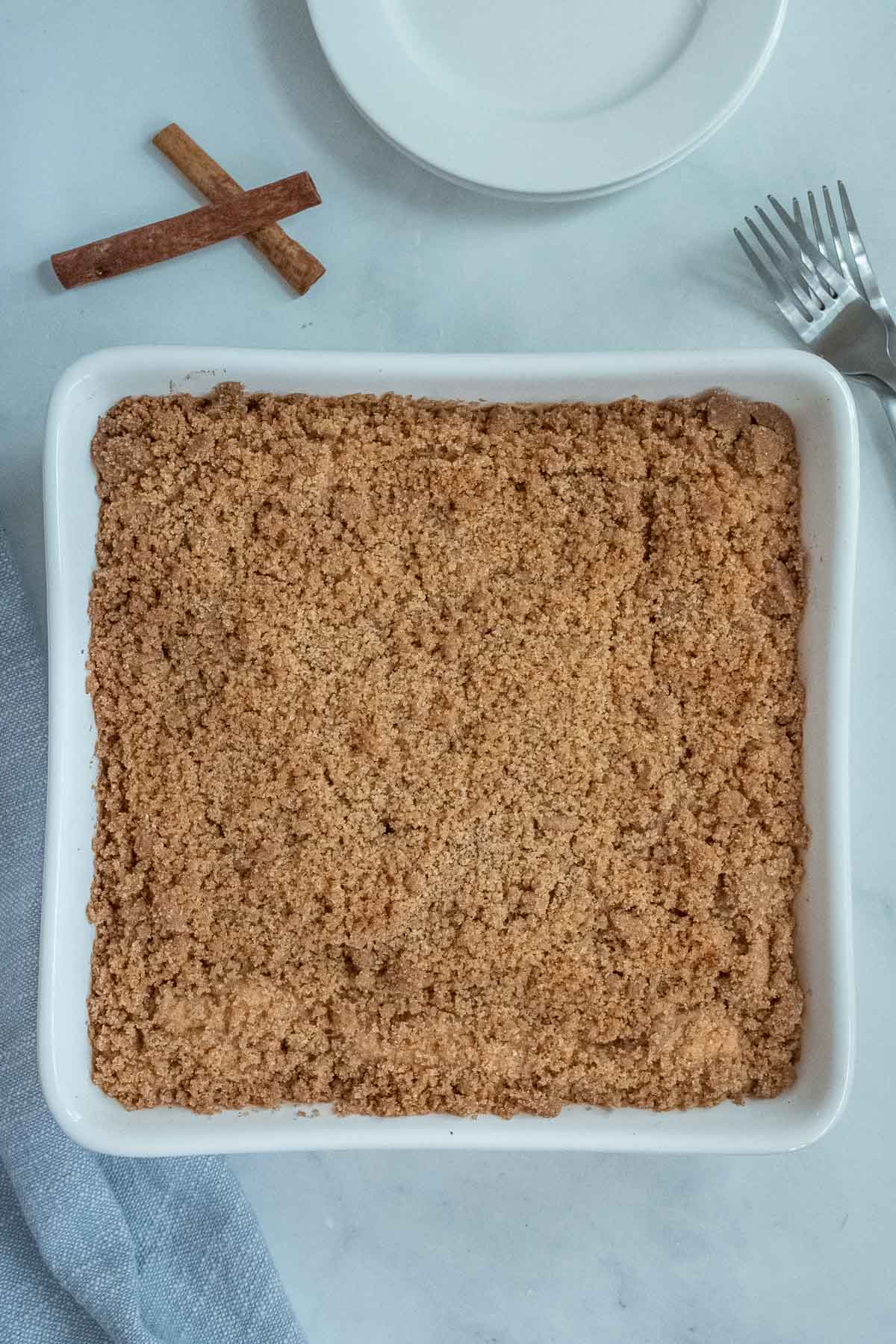 baked coffee cake in a square white baking dish with a blue napkin and white plates next to it