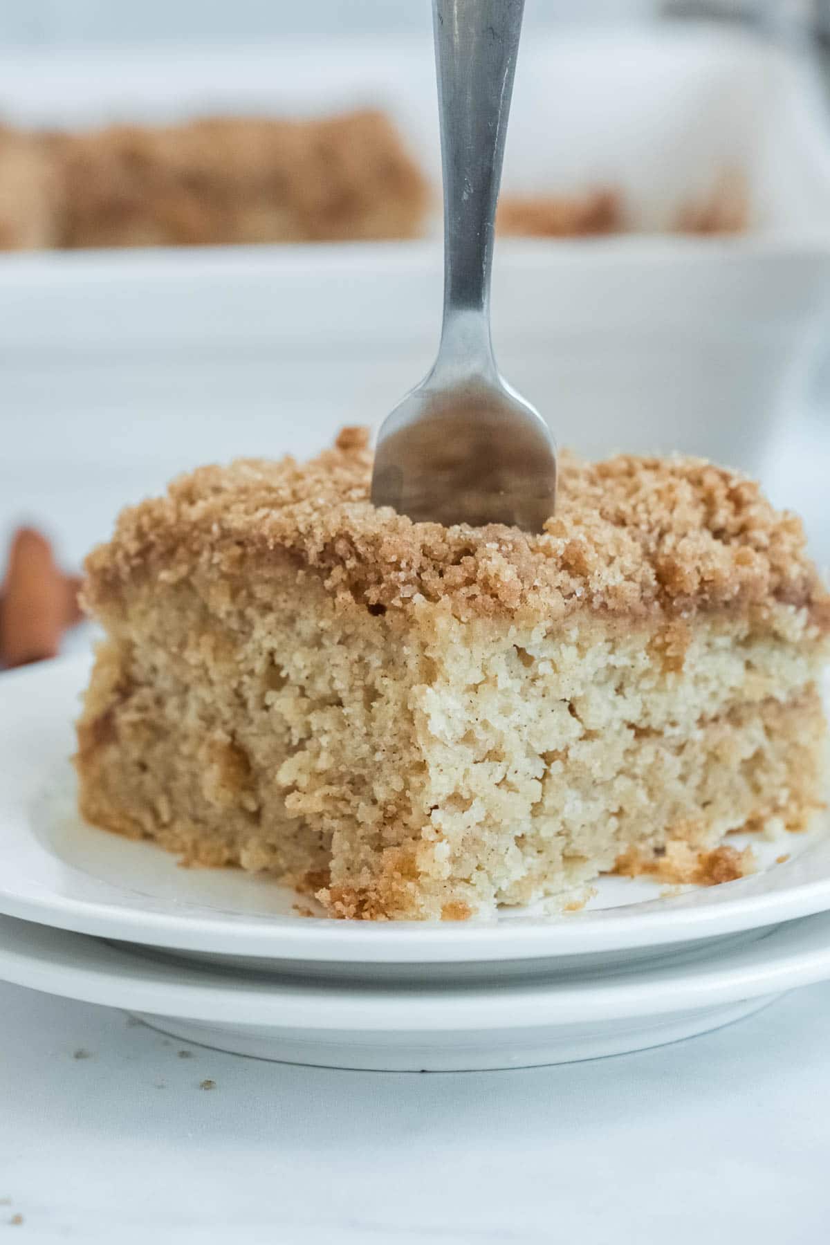 white plate with a square slice of coffee cake with a fork