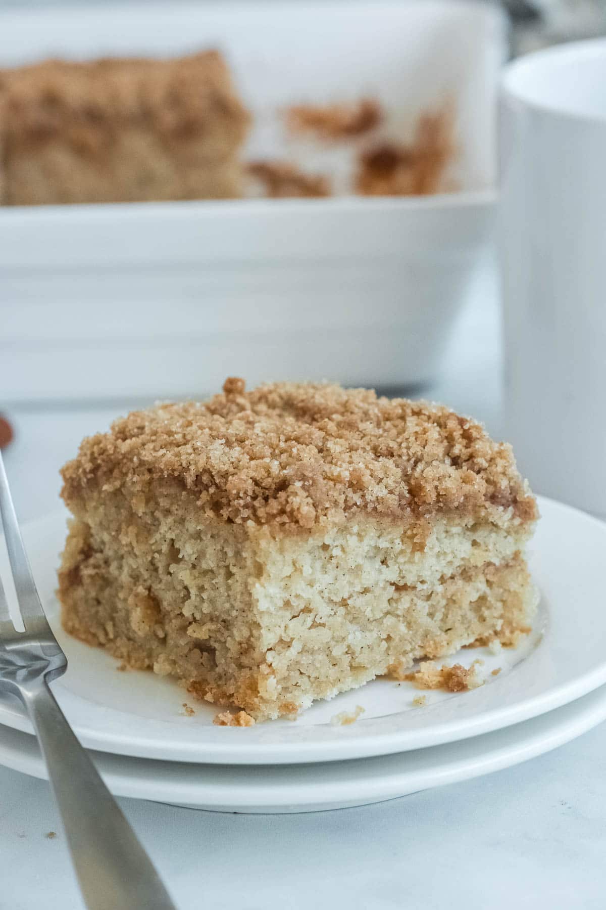 white plate with a square slice of coffee cake with a fork