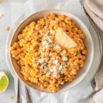 corn dip with cilantro and crumbled white cheese on top in a serving bowl