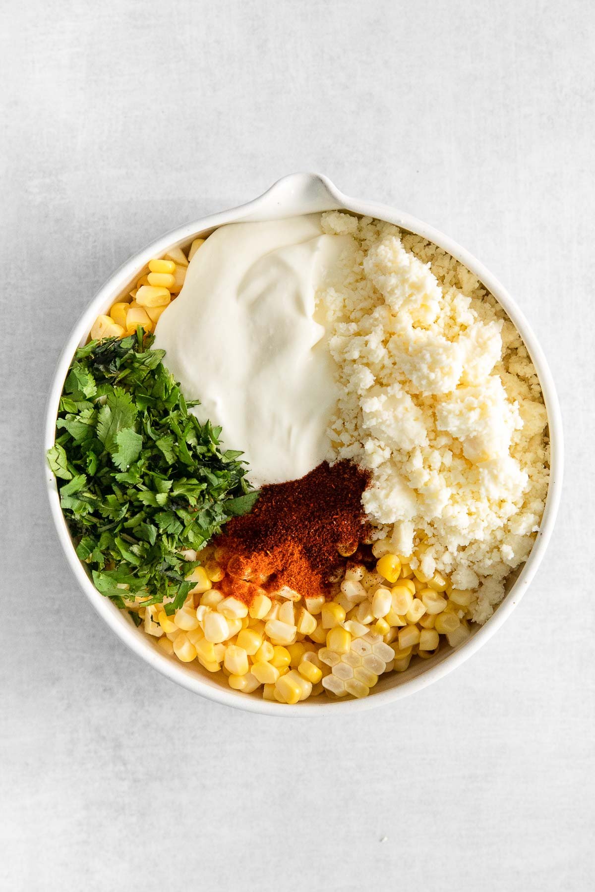 white bowl with corn kernels, cojito cheese, cilantro, sour cream, and chili powder in separated sections