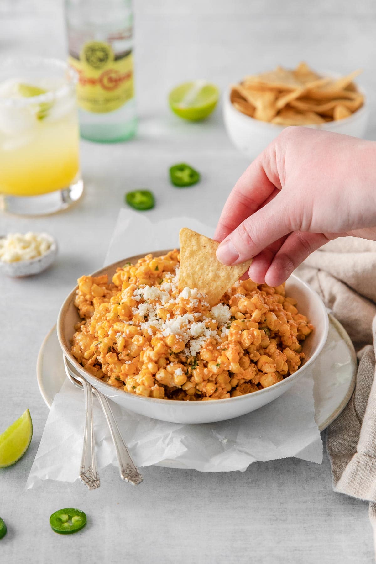 tortilla chip being dipped into corn dip that is topped with crumbled white cojito cheese