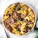 closeup of white bowl of beef stroganoff with egg noodles topped with parsley