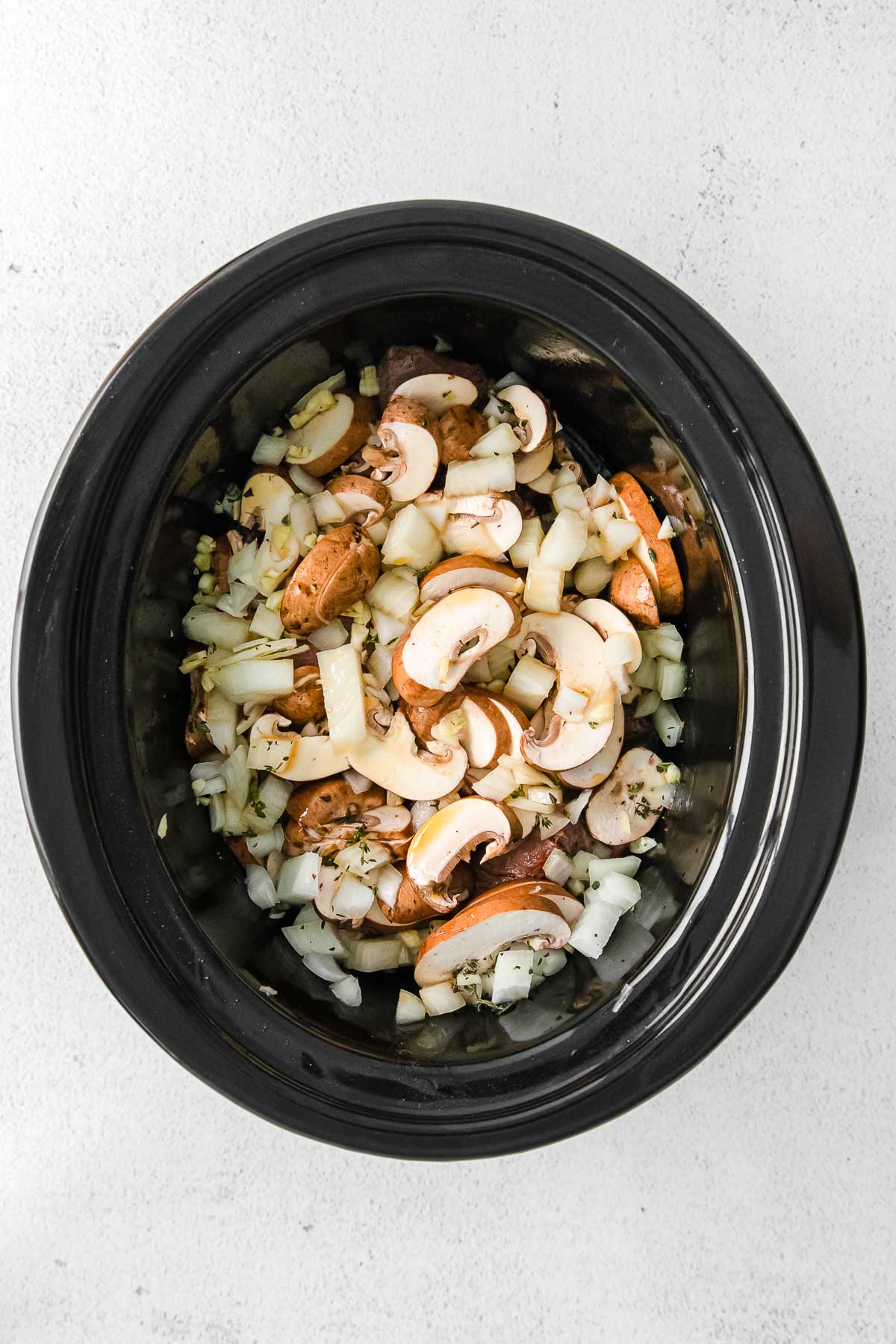 black crock pot with onions, mushrooms, thyme and beef broth