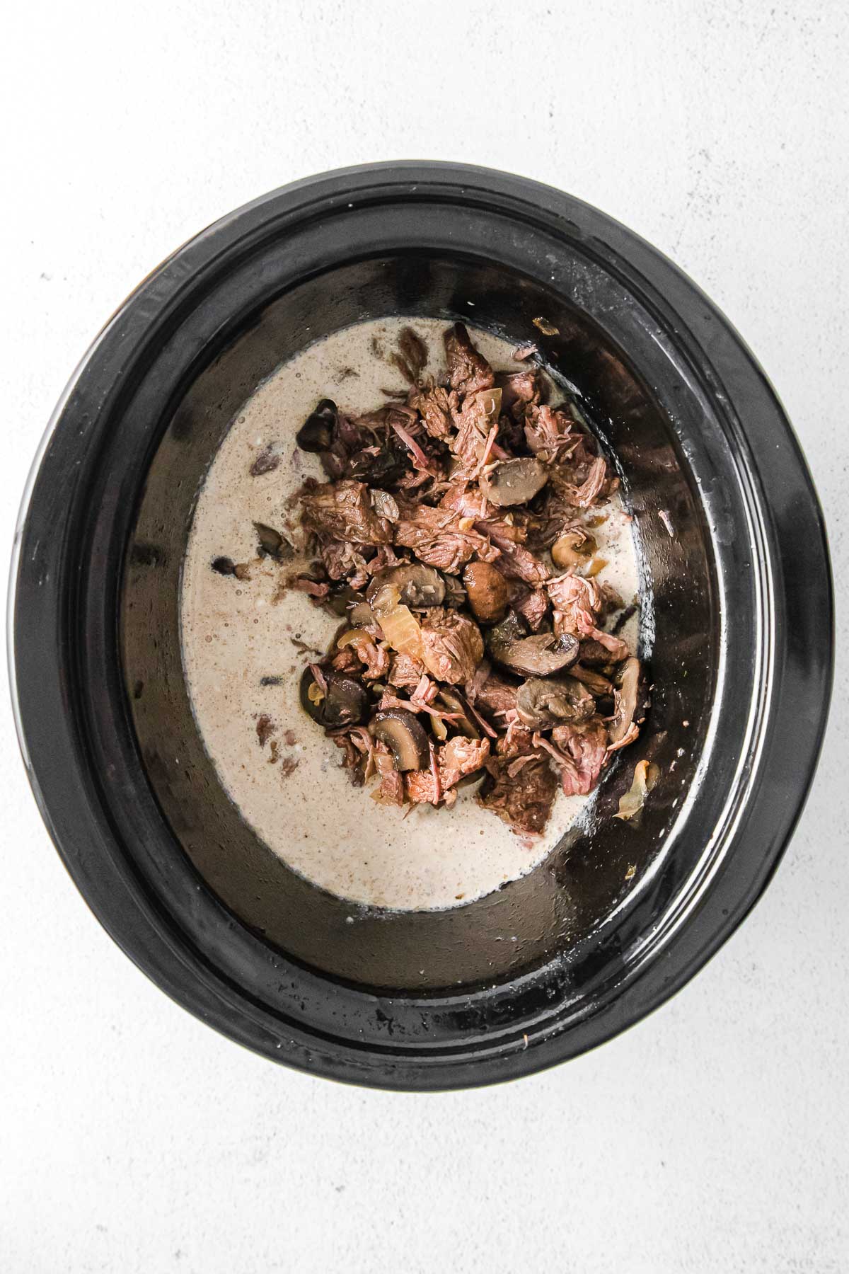 black slow cooker with creamy sauce with steak chunks