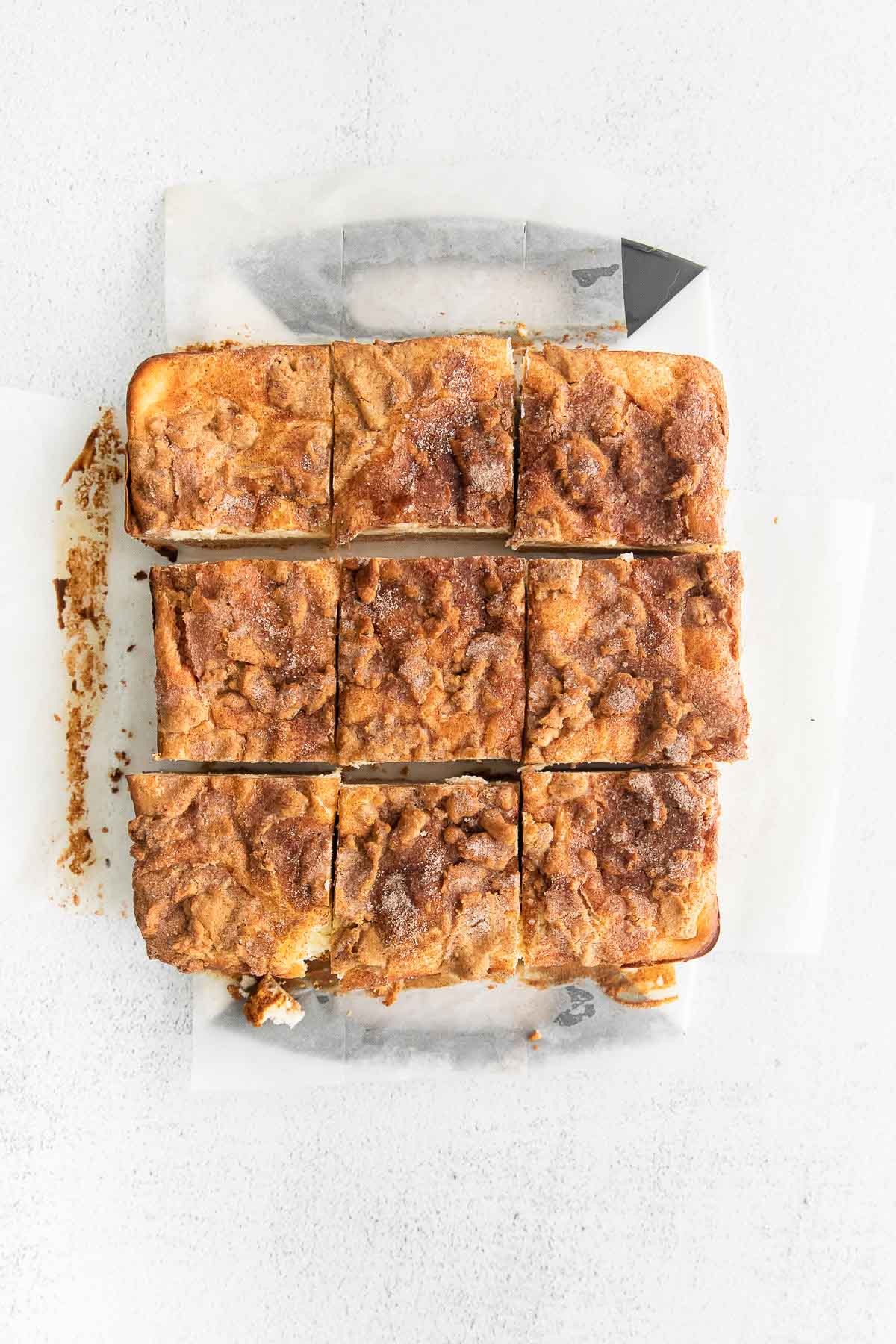 cheesecake bars with cinnamon sugar topping cut into 9 squares on a white cutting board