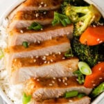 closeup of sliced pork chop with broccoli and carrots in a white bowl