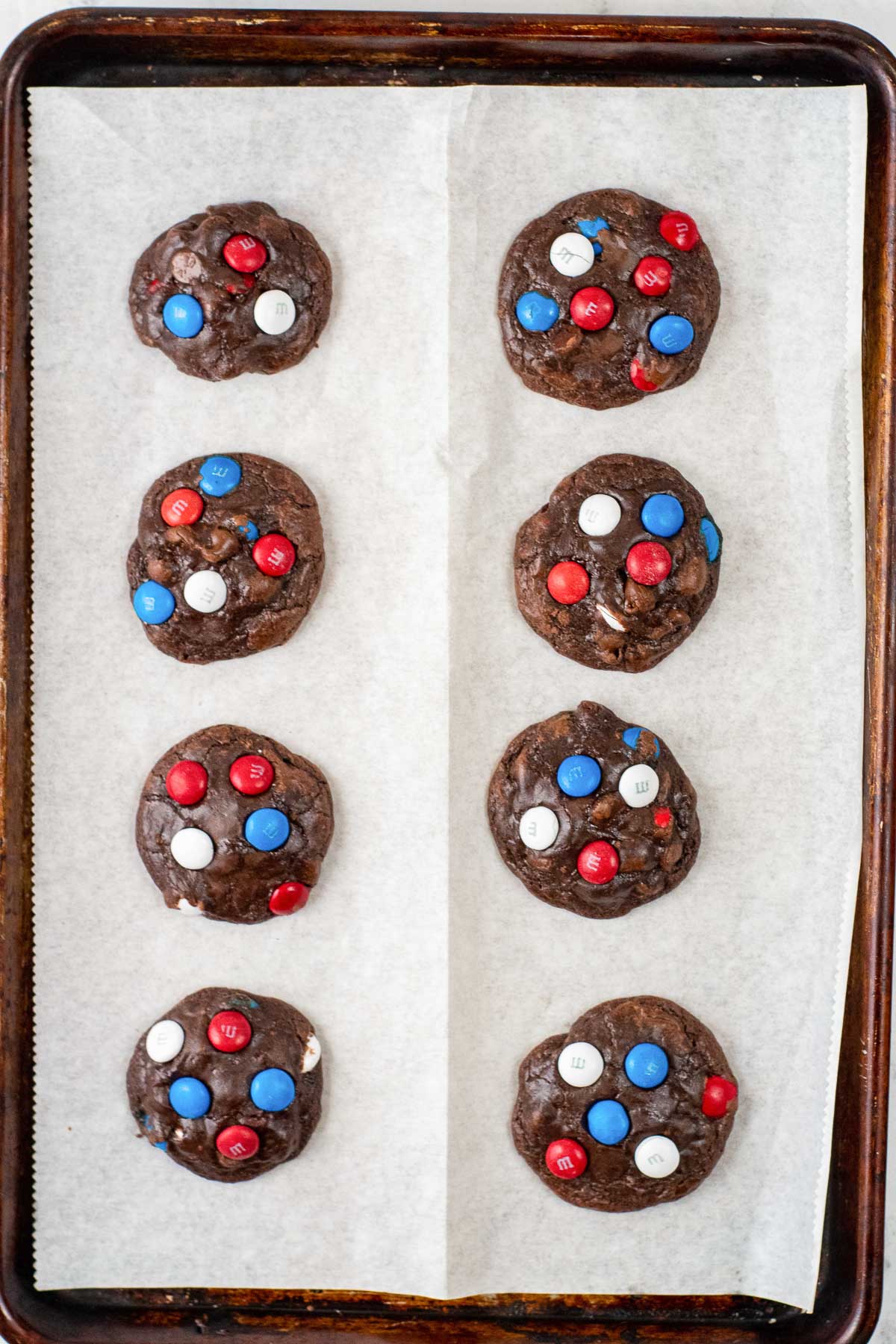 eight brownie cookies with red white and blue m&m's on a parchment paper lined cookie sheet