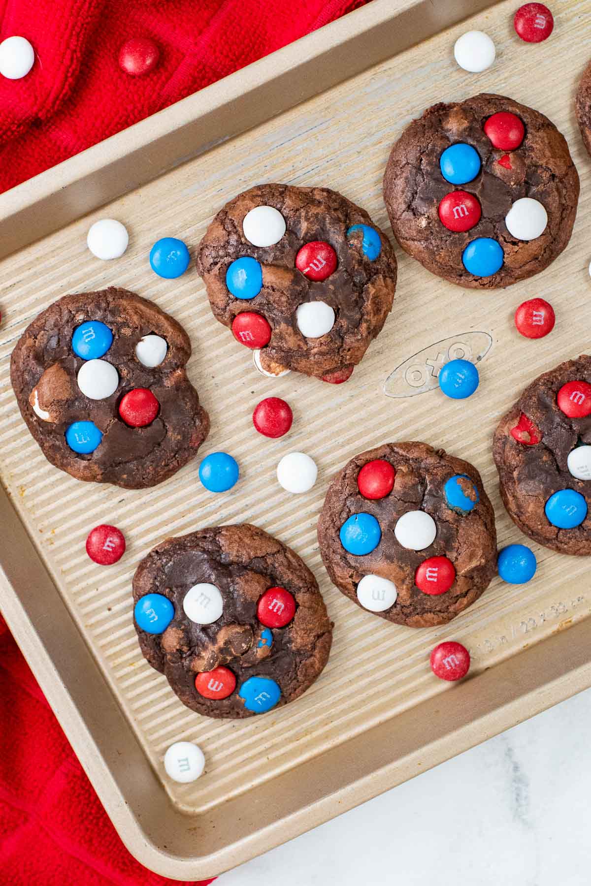 gold colored baking sheet with chocolate cookies with several red white and blue m&m candies