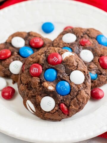white plate with three chocolate brownie cookies with red white and blue m&m's