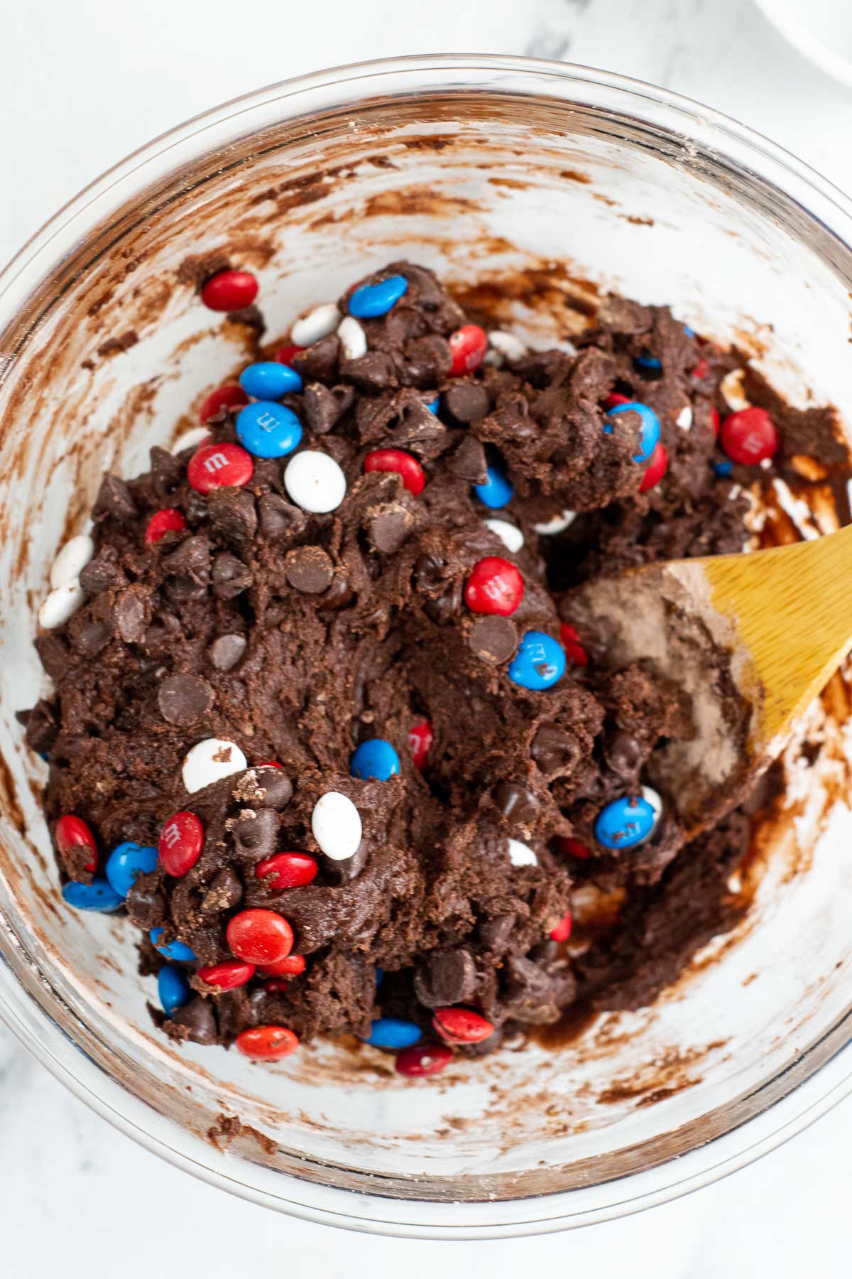 glass bowl with brownie cookie batter with red, white and blue m&m candies and chocolate chips mixed in