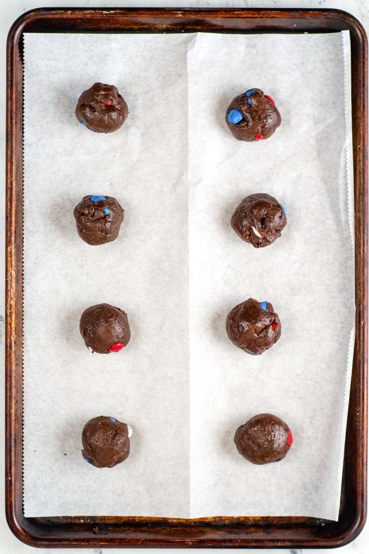eight balls of brownie cookie dough on a parchment lined baking sheet