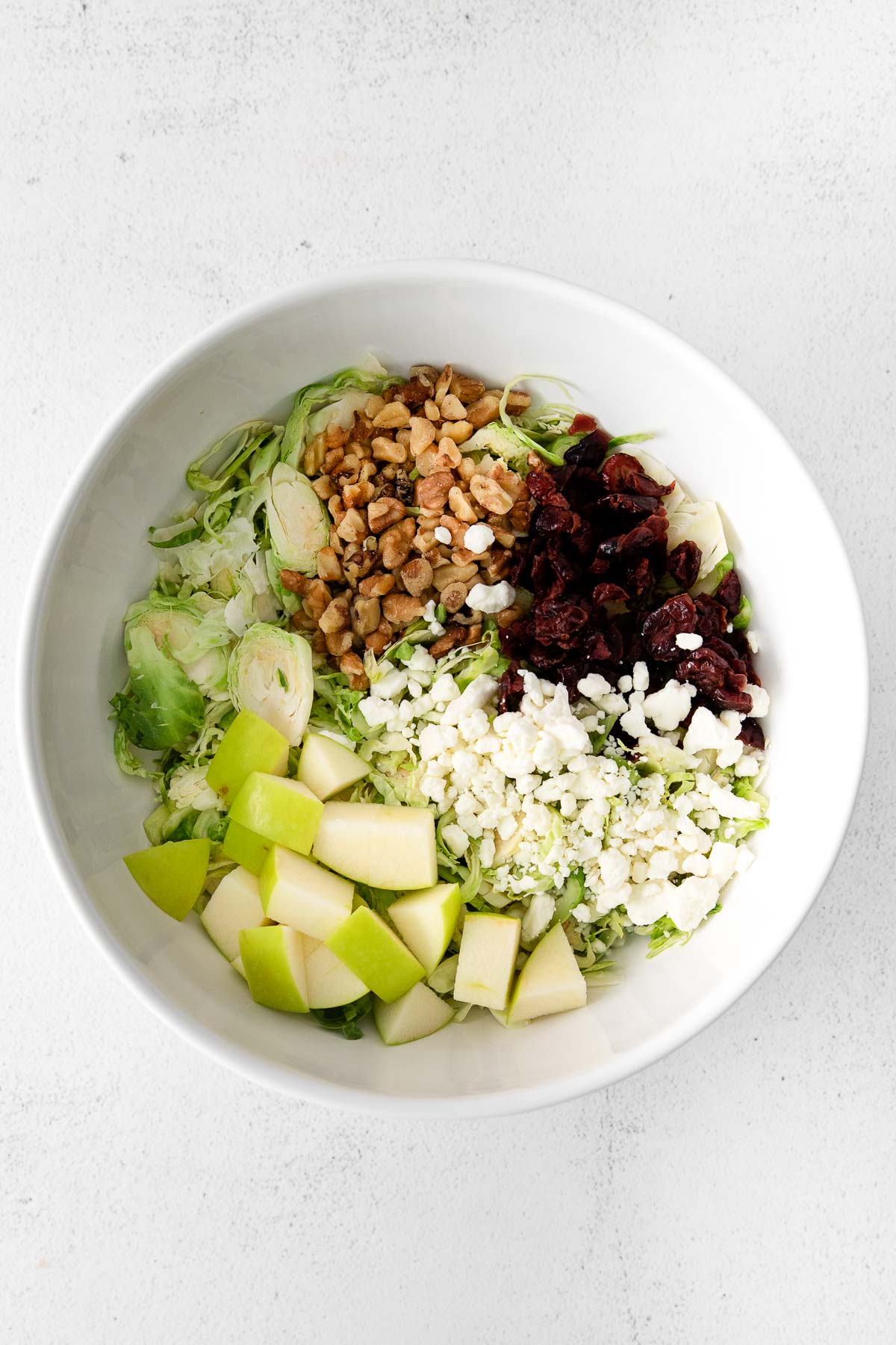 white serving bowl with diced green apples, feta cheese, cranberries, and walnuts divided in sections