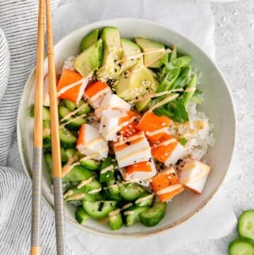 bowl full of fresh cucumber slices, imitaion crab meat, and avocado with spicy mayo drizzles and topped with sesame seeds