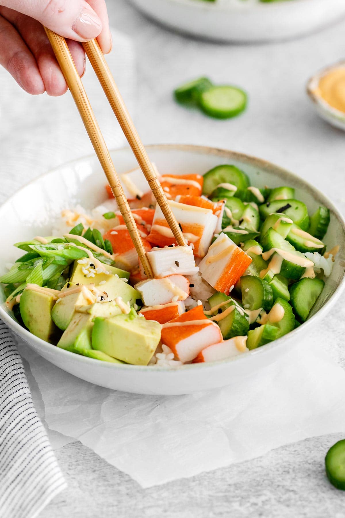 bowl with cucumber, crab meat, avocado with pink sauce drizzled over and chopsticks picking up a piece of crab meat
