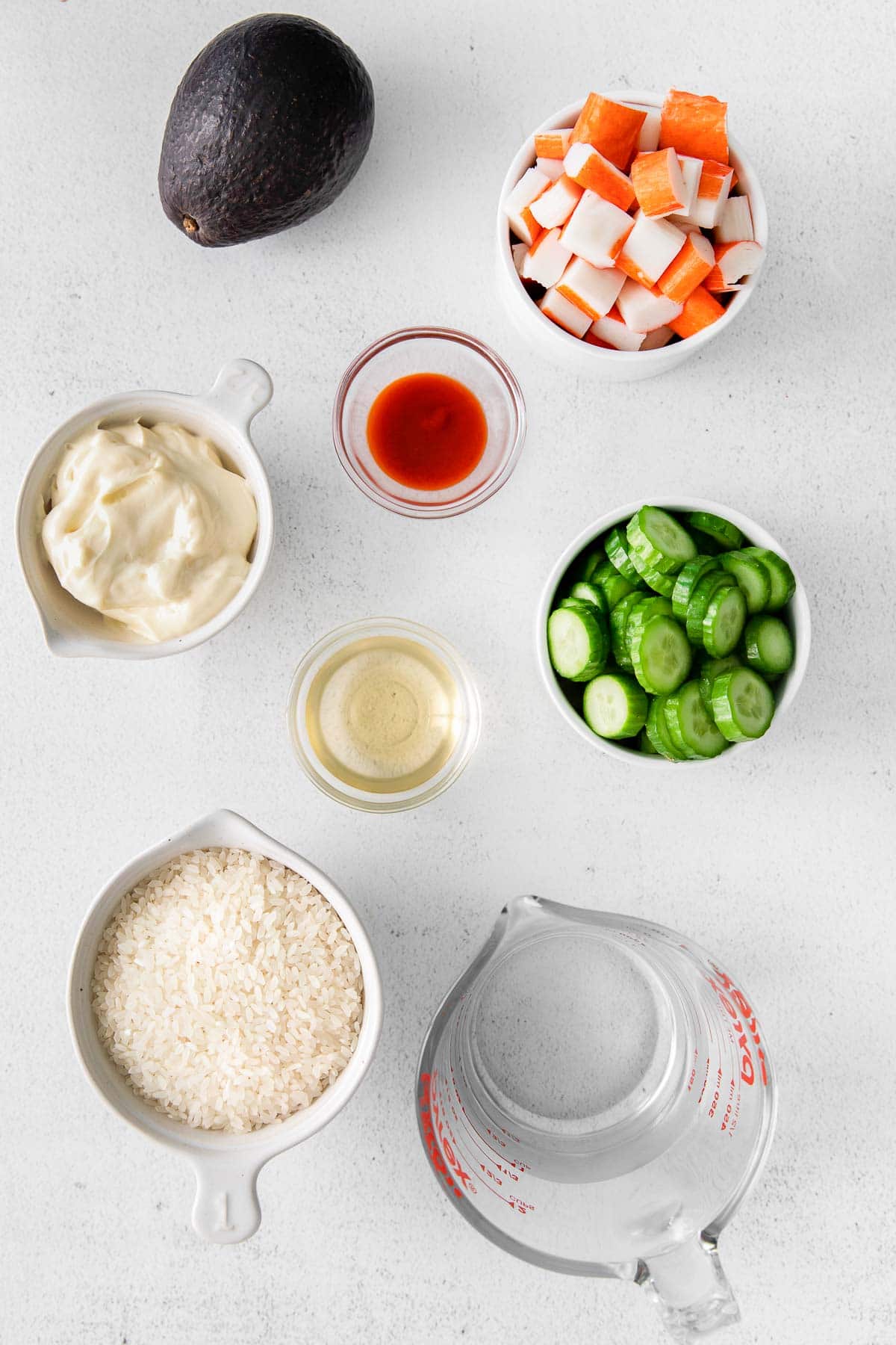 several bowls of ingredients for California roll sushi bowl - rice, cucumber, imitation crab meat, avocado, mayo, sriracha sauce