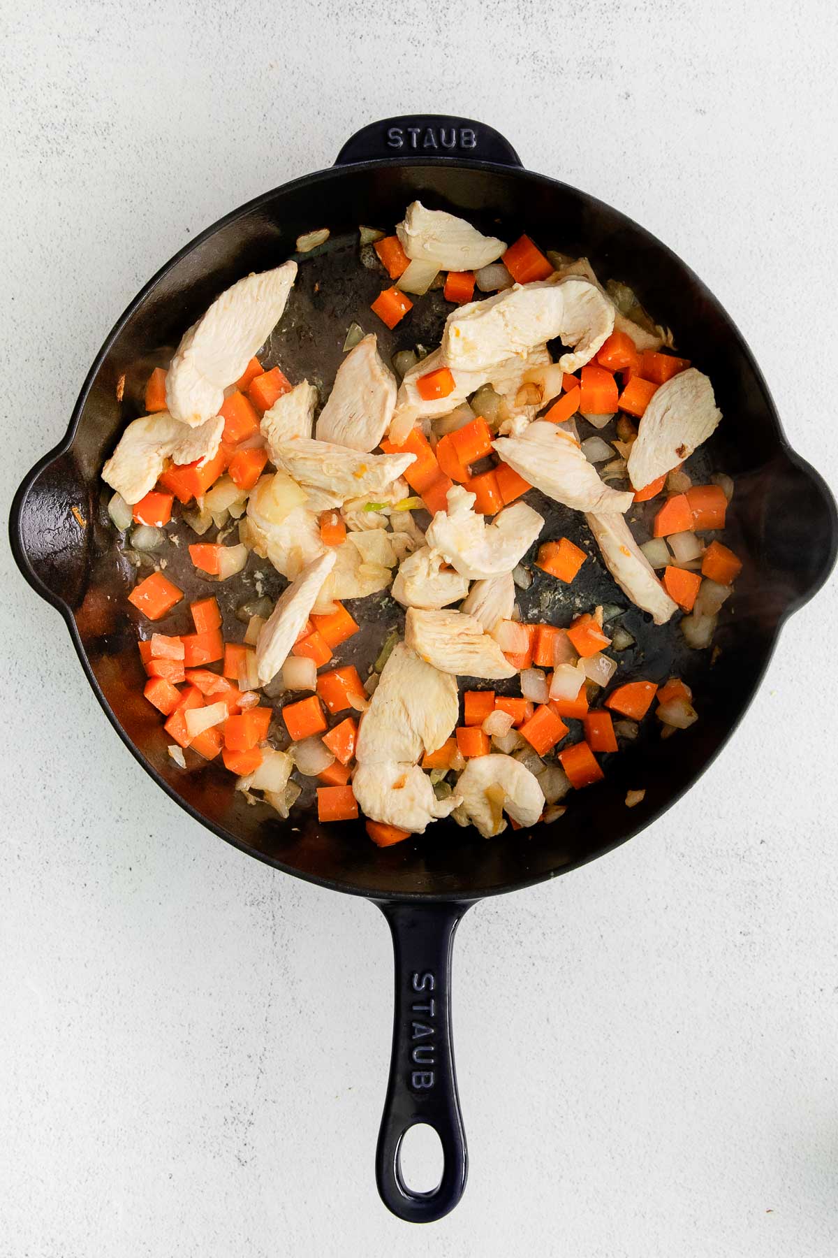 cast iron skillet with diced chicken, diced carrots and onions