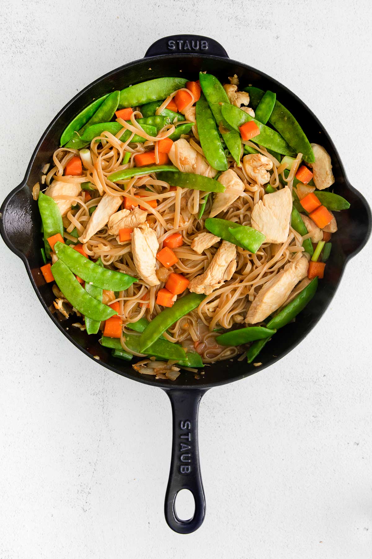 cast iron skillet with snow peas, sliced chicken, diced carrots and rice noodles