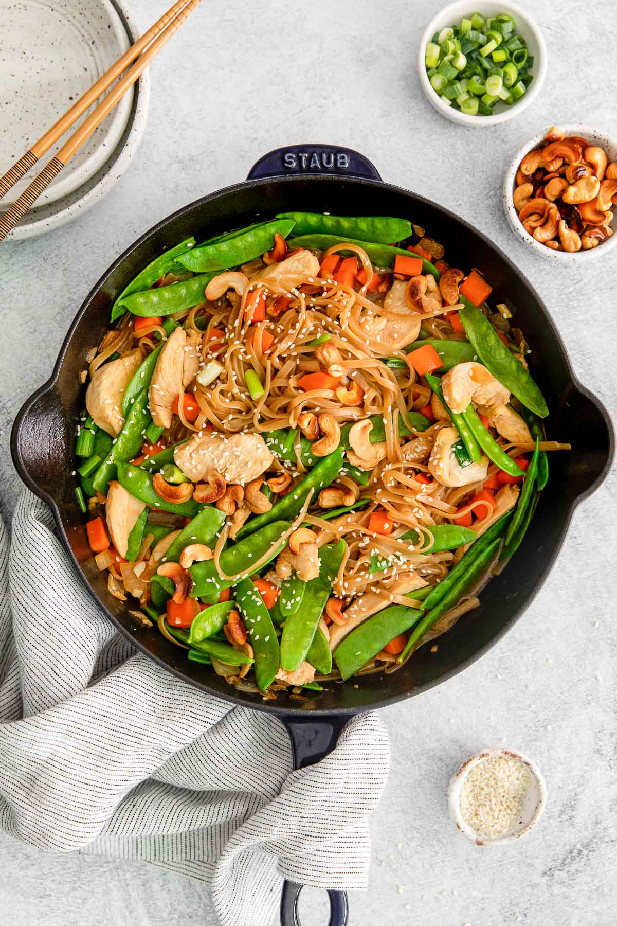 black cast iron skillet with cashew chicken stir fry tossed with rice noodles snow peas, carrots topped with sesame seeds