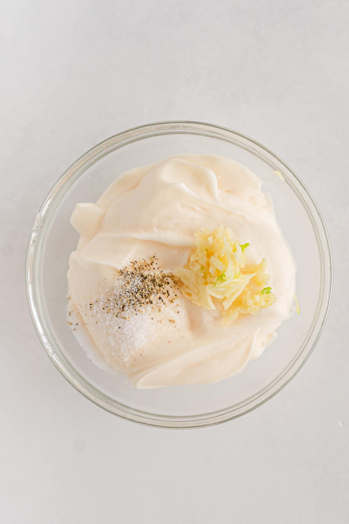 small glass bowl with mayonnaise topped with minced garlic, salt and pepper