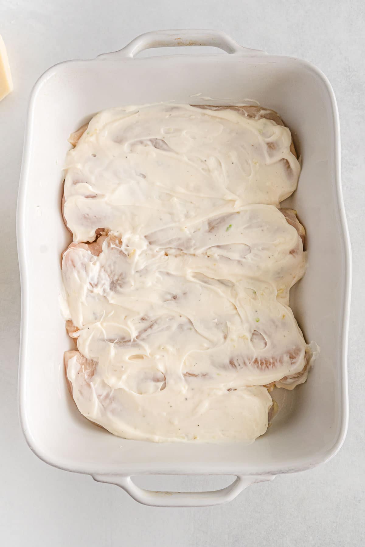 white casserole dish with chicken breasts topped with mayonnaise