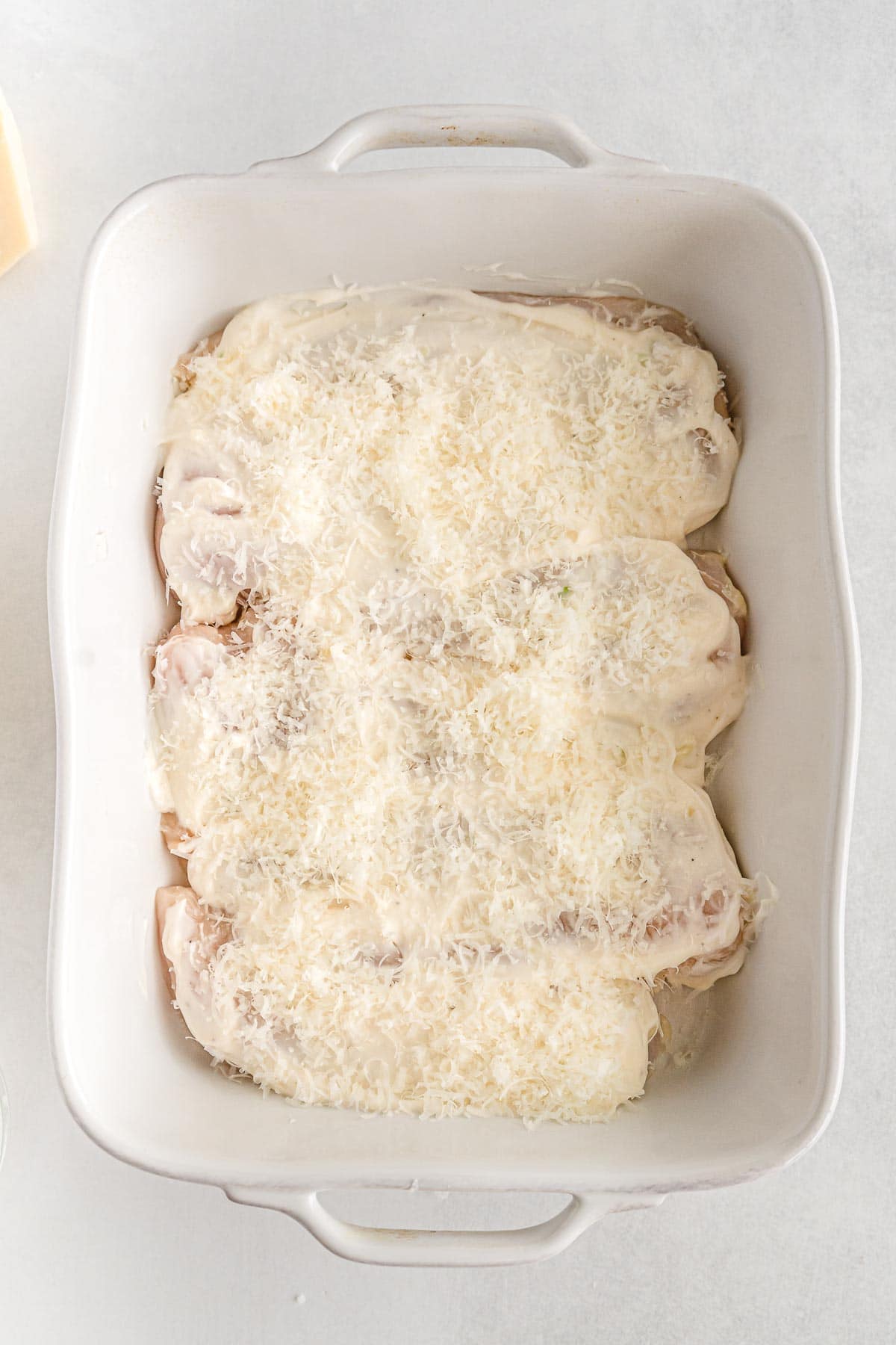 white casserole dish with chicken breasts topped with mayonnaise and parmesan cheese