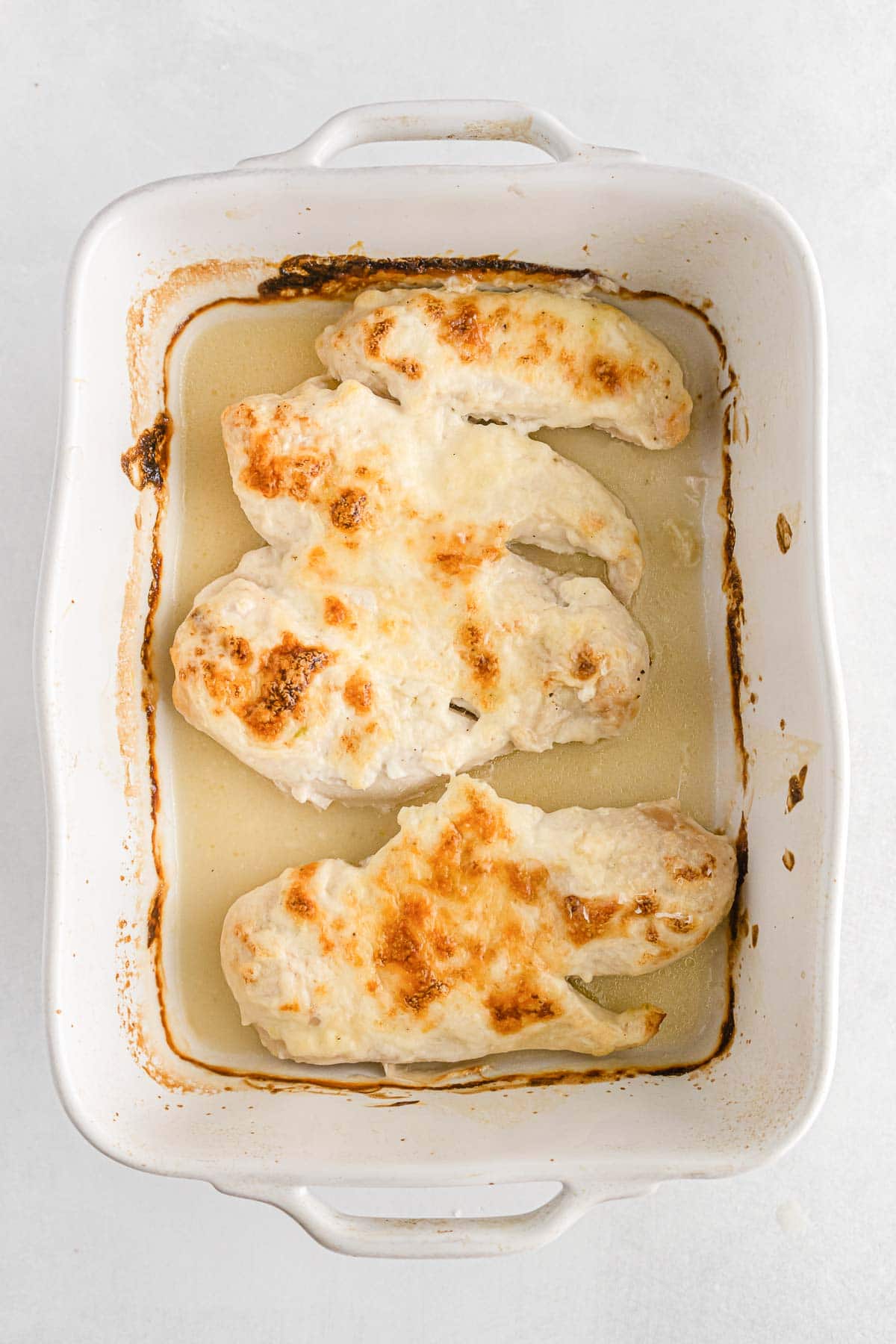 baked chicken breasts topped with parmesan crust in a white casserole dish
