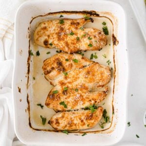 white casserole with four baked chicken breasts topped with parmesan cheese and fresh parsley