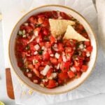 closeup of pico de gallo in a white bowl with 2 tortilla chips dipped in