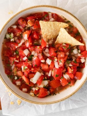 closeup of pico de gallo in a white bowl with 2 tortilla chips dipped in