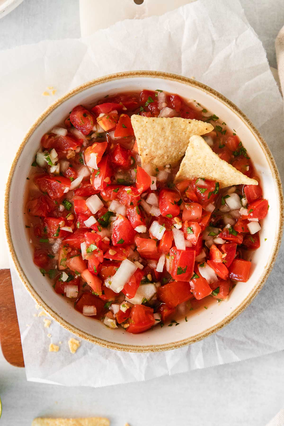bowl of pico de gallo dip in a white serving bowl with two tortilla chips dipped in