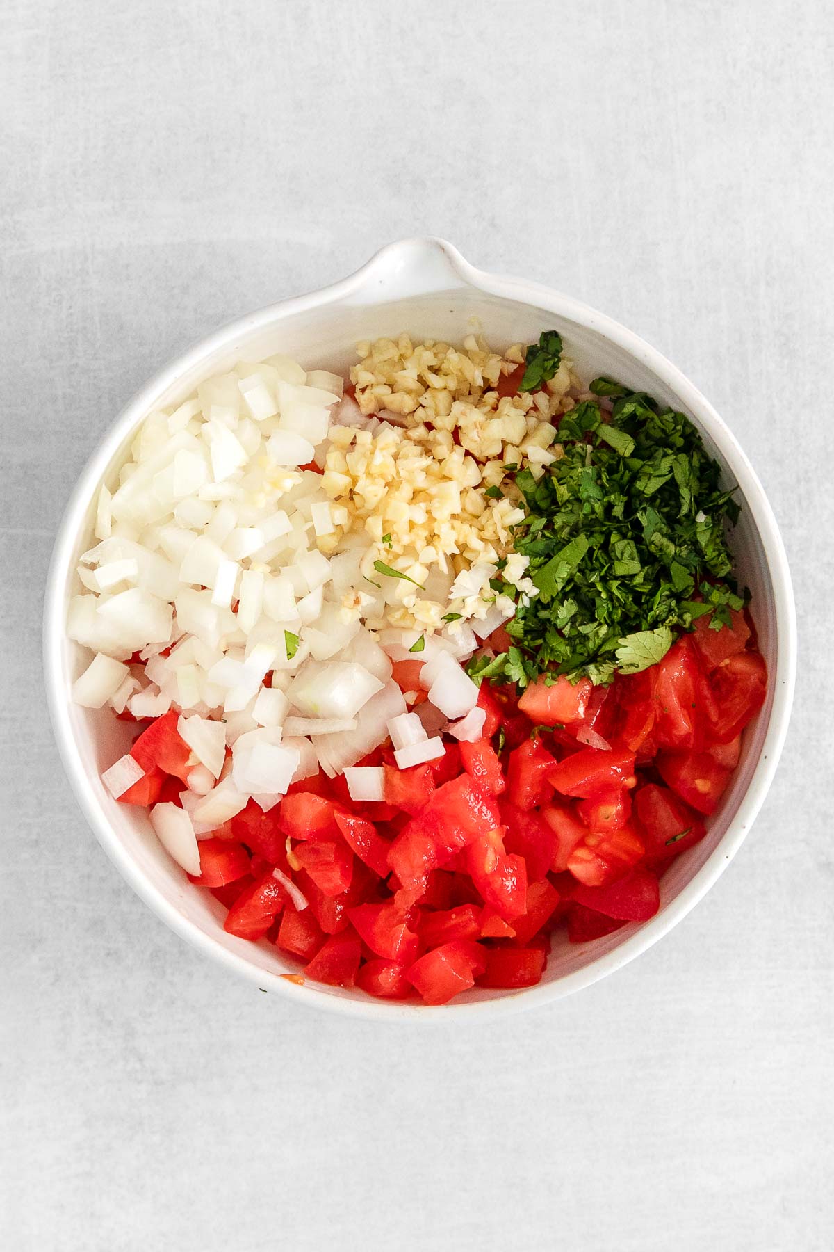 white bowl with diced tomatoes, onion, cilantro and garlic