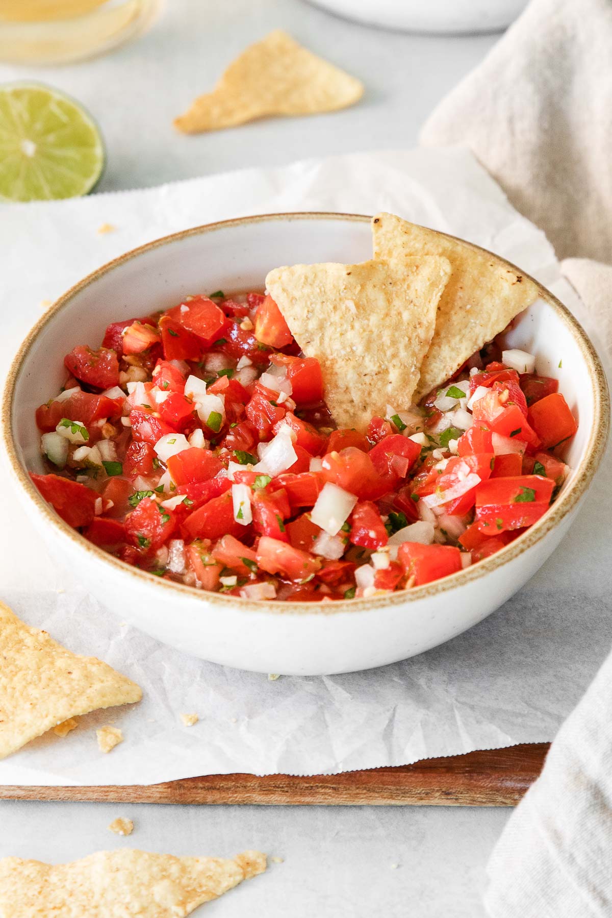 white bowl with pico de gallo tomato dip with two tortilla chips dipped in